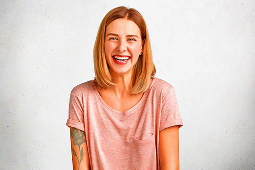 Positive adorable woman who has tattooed arm smiles gently at camera.